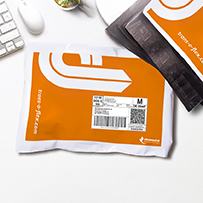 Orange Versandtasche mit trans-o-flex Logo und Label auf einem Schreibtisch